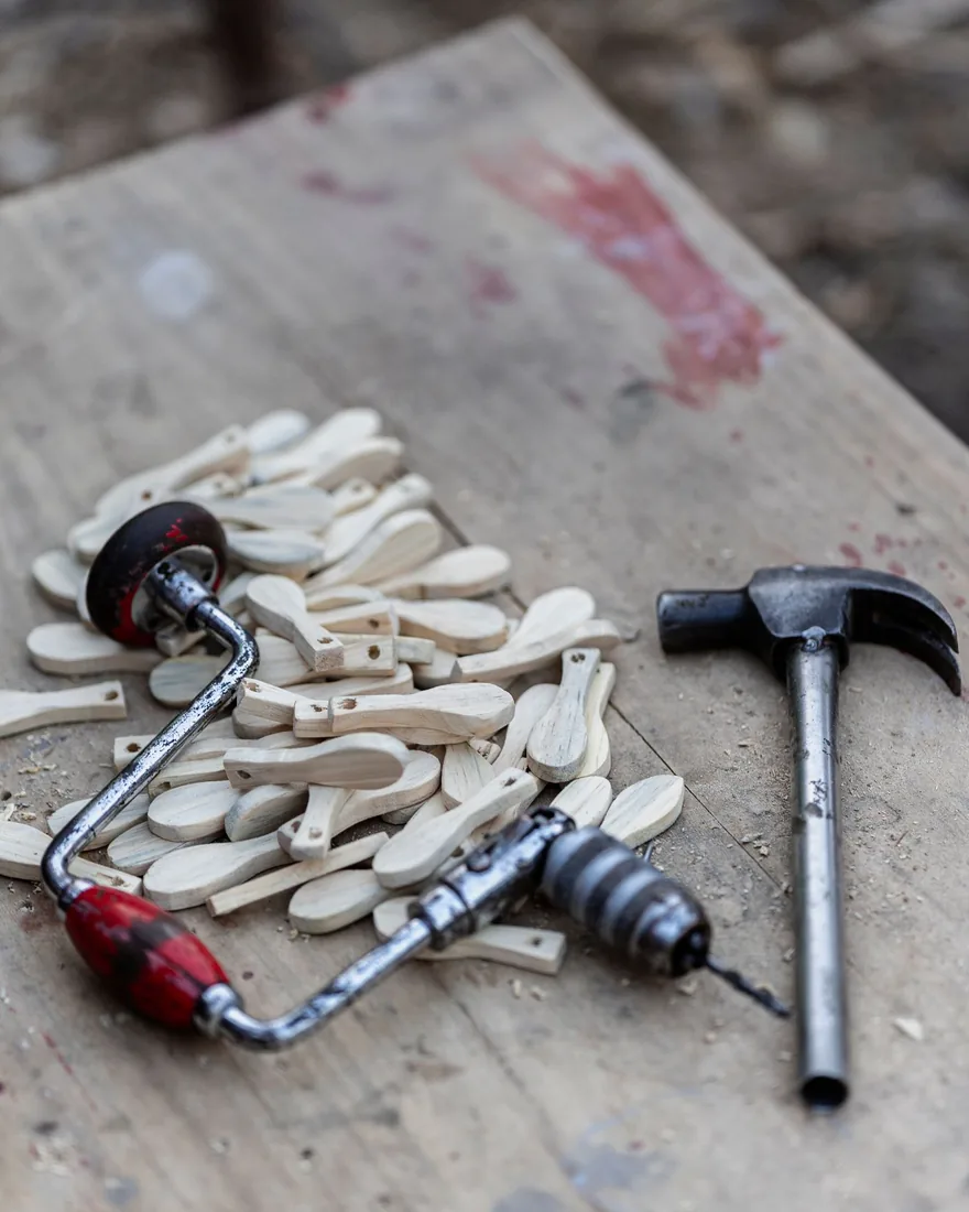 Piezas de madera clara sin terminar junto a un berbiquí y un martillo sobre un banco de taller